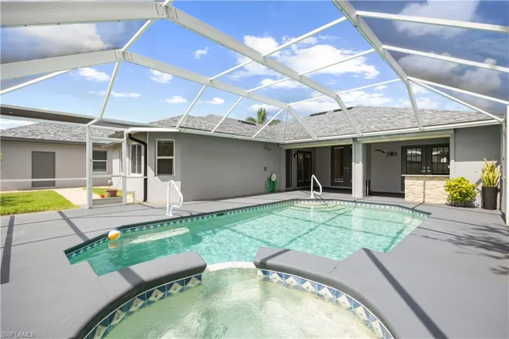 Screened outdoor pool area featuring a rectangular swimming pool, integrated spa, ample deck space, and a stone-finish outdoor bar