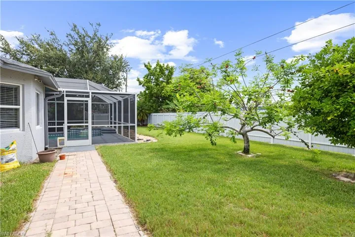 Expansive backyard featuring a green lawn, mature trees, and a white fence