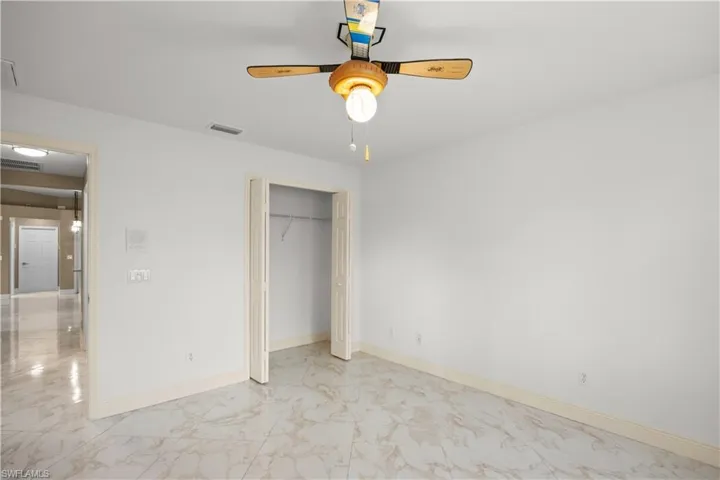 Spacious room featuring light-toned walls, marble-finish flooring, a ceiling fan with integrated lighting, and an open closet