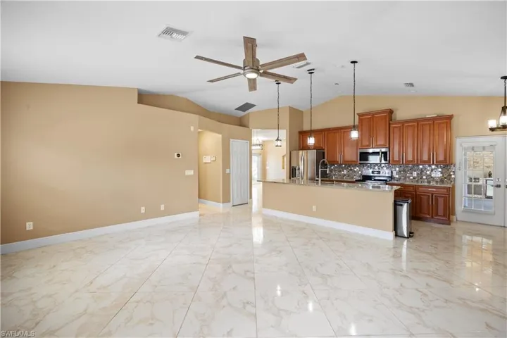Spacious open-concept living area featuring large format porcelain tile flooring, vaulted ceilings, and an integrated kitchen with wood cabinetry