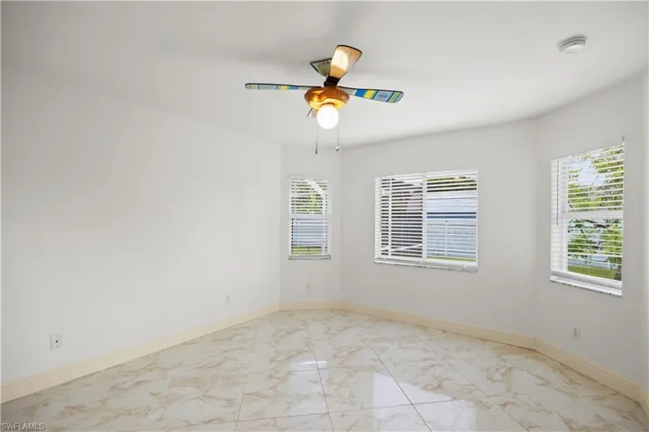 Spacious room featuring light-toned large format tile flooring, three windows with horizontal blinds, a ceiling fan with integrated lighting, and white baseboards