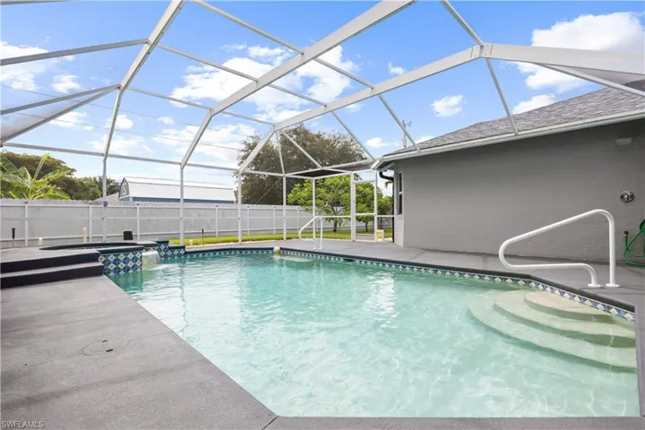 Screened-in swimming pool featuring integrated steps, decorative tile accents, and a raised spa with a water feature