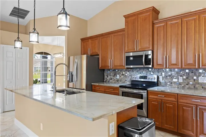 Kitchen featuring a central island with a light-toned countertop, stainless steel appliances, wood-finish cabinetry, and a mosaic tile backsplash