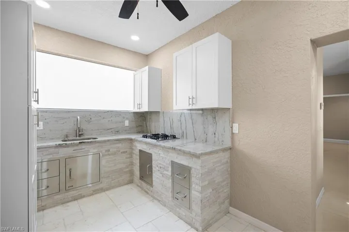 Outdoor kitchen featuring a built-in gas cooktop, integrated stainless steel appliances, stone tile backsplash, white shaker-style cabinetry, and tiled flooring