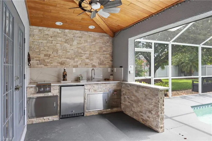 Outdoor summer  kitchen featuring stacked stone finishes and a wood-finish vaulted ceiling