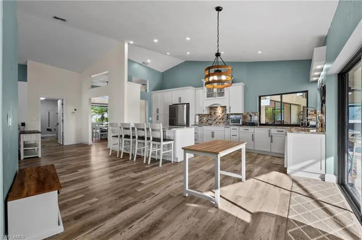 Kitchen with refrigerator, high vaulted ceiling, white cabinets, wood finished floors, and tasteful backsplash