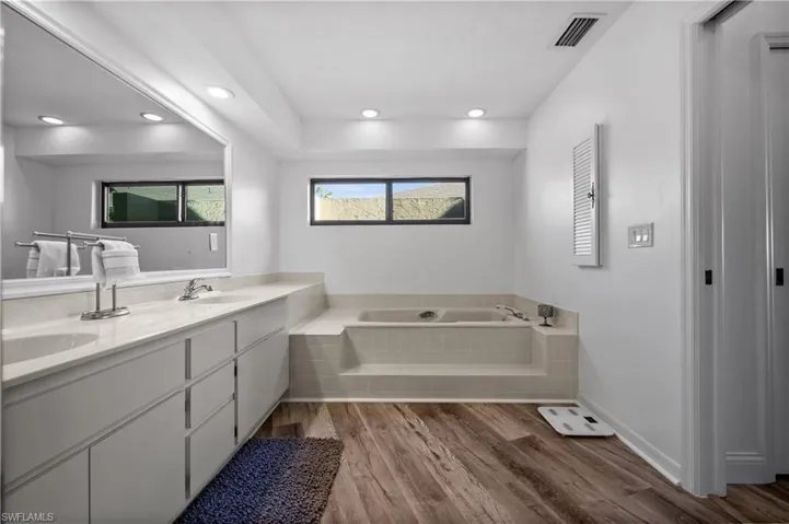 Full bath featuring wood finished floors, a bath, double vanity, and recessed lighting