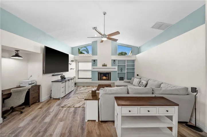 Living area featuring a ceiling fan, high vaulted ceiling, light wood-style flooring, a fireplace,
