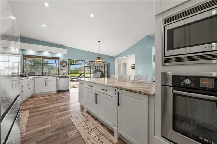 Kitchen with appliances with stainless steel finishes, wood-style floors, vaulted ceiling, white cabinets, and light stone counters