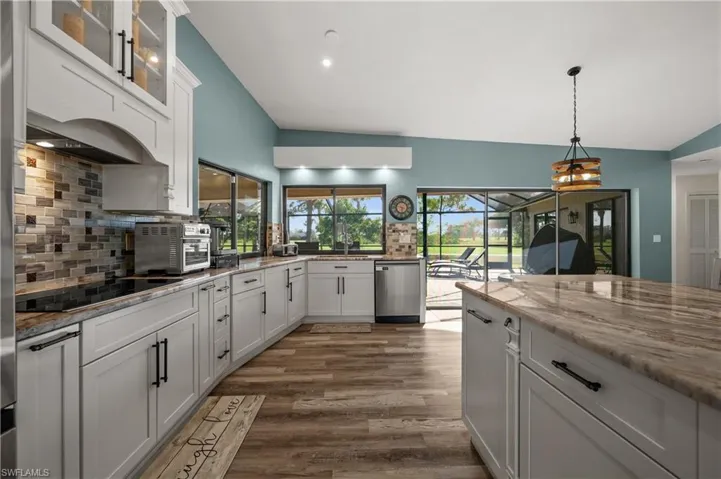 Kitchen featuring black electric stovetop, vaulted ceiling, dishwasher, decorative backsplash, and wood-style flooring