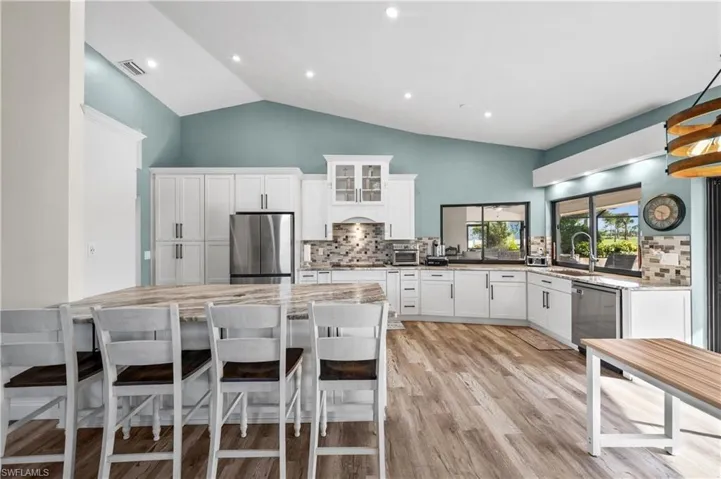 Kitchen with appliances with stainless steel finishes, a sink, tasteful backsplash, white cabinetry, and high vaulted ceiling