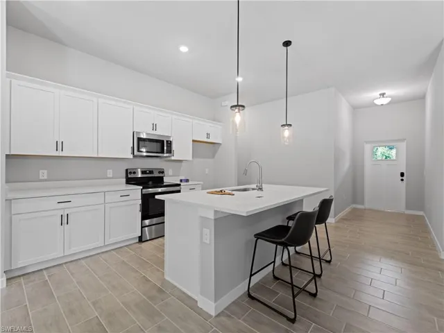 Kitchen with hanging light fixtures, white cabinets, a kitchen island with sink, and appliances with stainless steel finishes