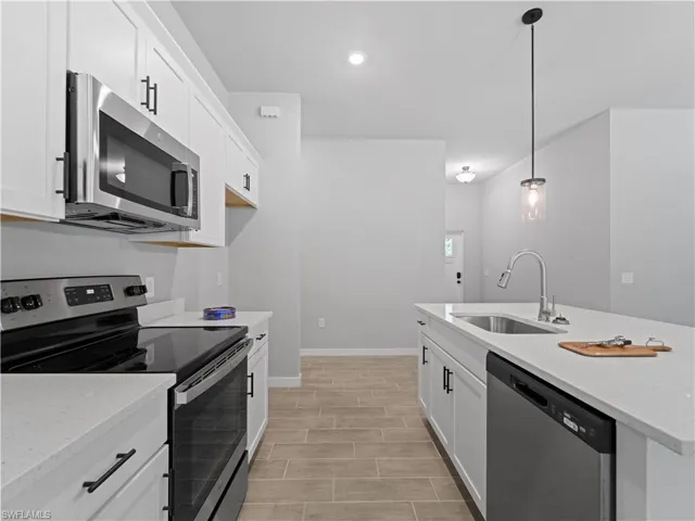 Kitchen with light stone countertops, stainless steel appliances, pendant lighting, sink, and white cabinetry
