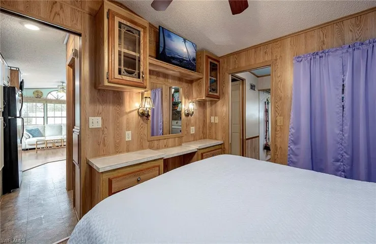 Bedroom with wooden walls, a textured ceiling, freestanding refrigerator, and ceiling fan