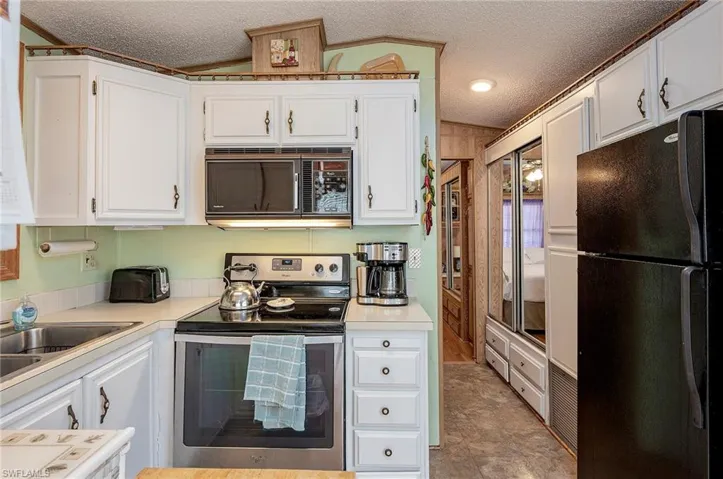 Kitchen with black appliances, light countertops, white cabinets, and a textured ceiling