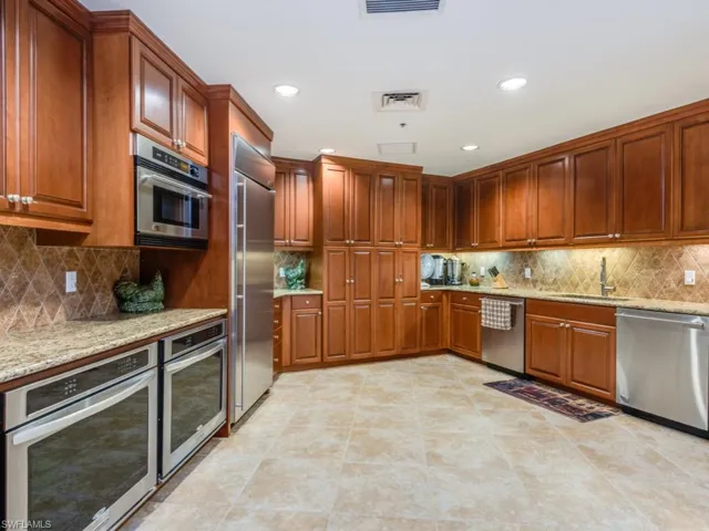 Kitchen featuring appliances with stainless steel finishes, backsplash, light stone counters, recessed lighting, and brown cabinetry