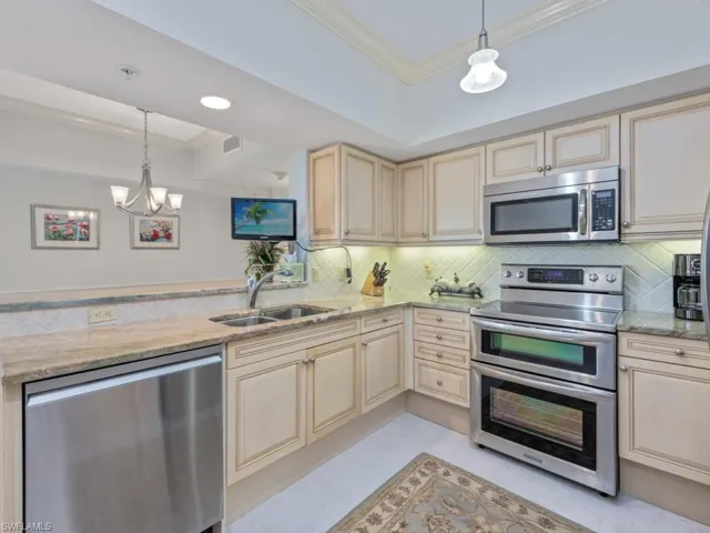 Kitchen featuring stainless steel appliances, cream cabinetry, crown molding, a chandelier, and light stone countertops