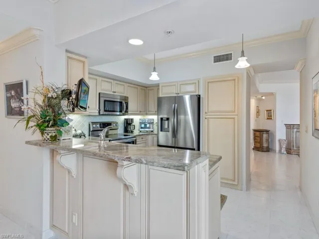Kitchen featuring stainless steel appliances, cream cabinetry, a peninsula, decorative backsplash, and ornamental molding