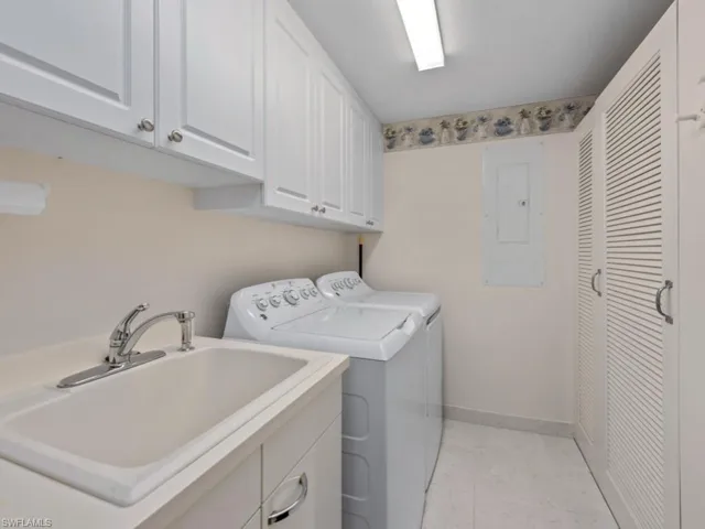Washroom featuring cabinet space, washing machine and clothes dryer, electric panel, and light marble finish flooring
