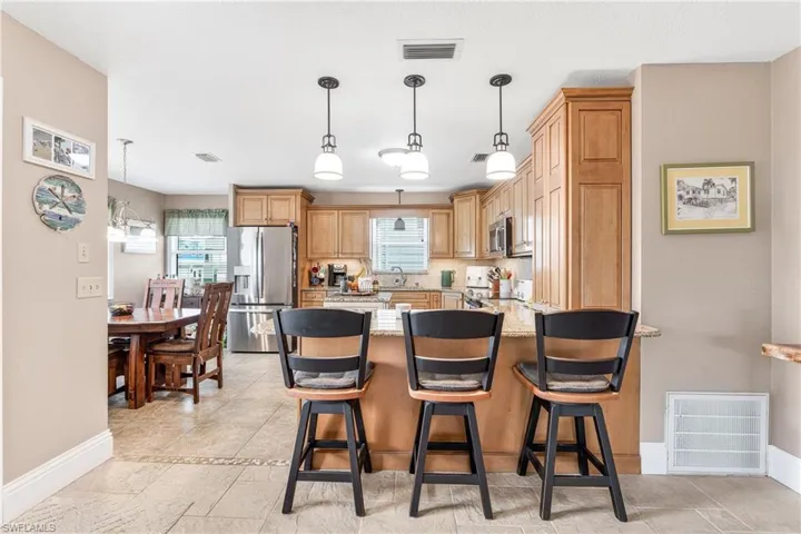 Kitchen with decorative light fixtures, stainless steel appliances, a kitchen breakfast bar, light stone counters, and a peninsula