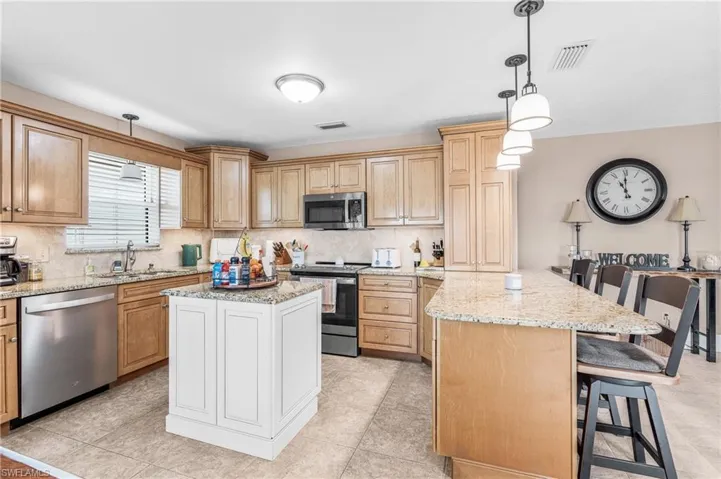 Kitchen with a kitchen bar, pendant lighting, stainless steel appliances, light stone countertops, and backsplash