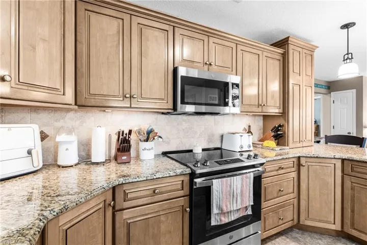 Kitchen featuring appliances with stainless steel finishes, light stone counters, pendant lighting, backsplash, and brown cabinetry