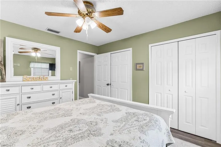 Bedroom with two closets, a textured ceiling, dark wood finished floors, and ceiling fan
