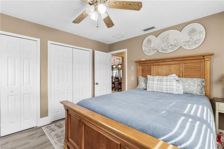 Bedroom with multiple closets, light wood-type flooring, a textured ceiling, and a ceiling fan
