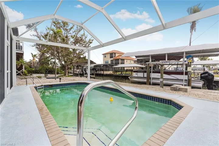 Swimming pool featuring boat lift, a water view, a dock, a patio area, and a sunroom