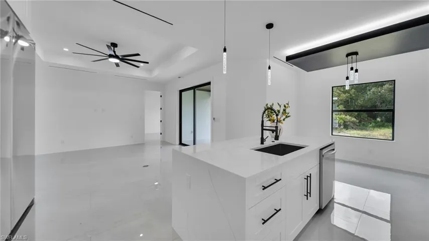 Kitchen with an island with sink, light stone counters, hanging light fixtures, white cabinetry, and recessed lighting