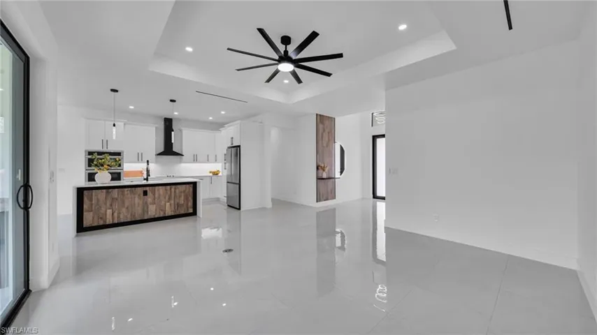 Unfurnished living room with a ceiling fan, a raised ceiling, recessed lighting, and light tile patterned floors