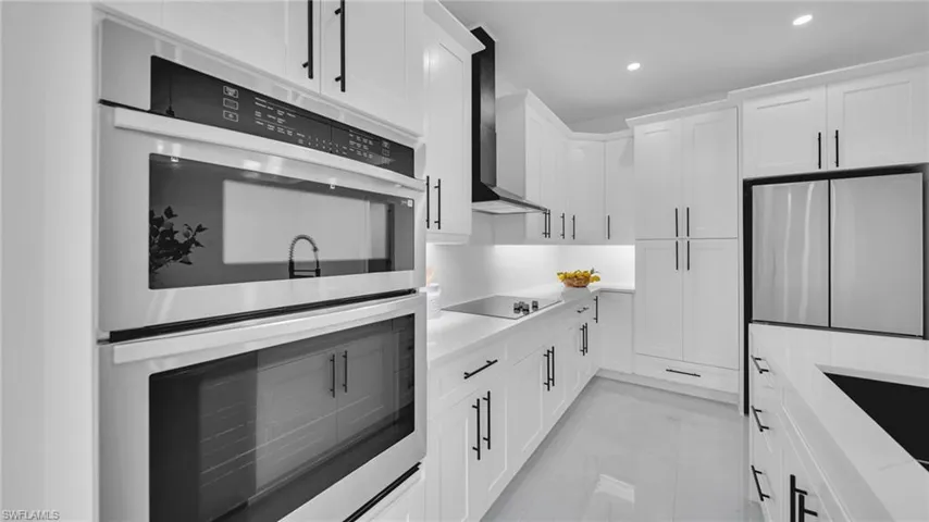 Kitchen with stainless steel appliances, white cabinetry, recessed lighting, wall chimney range hood, and light marble finish flooring