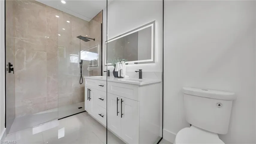 Bathroom featuring double vanity, tiled shower, and recessed lighting