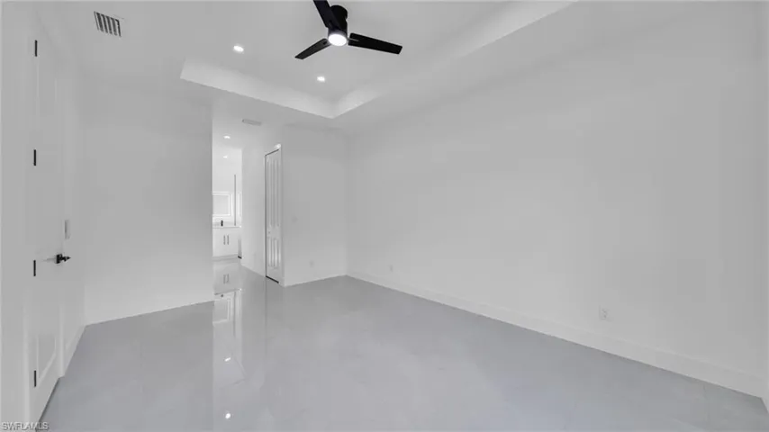Unfurnished bedroom with recessed lighting, a tray ceiling, connected bathroom, and ceiling fan