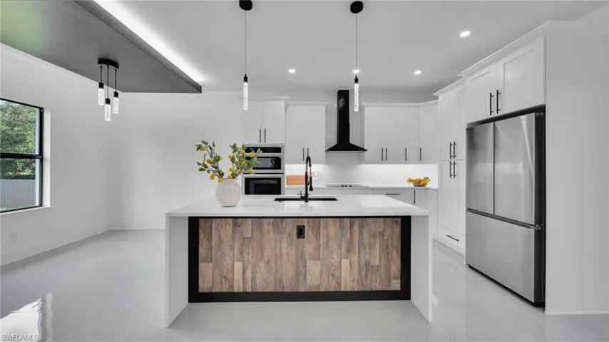 Kitchen featuring freestanding refrigerator, wall chimney exhaust hood, light countertops, white cabinetry, and recessed lighting