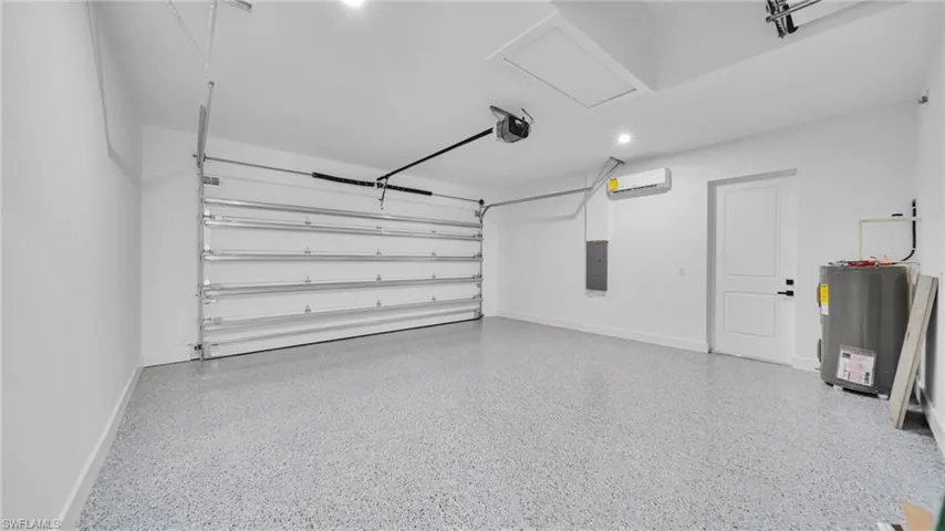 Garage with electric water heater, electric panel, recessed lighting, a wall unit AC, and a garage door opener