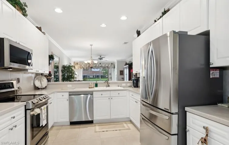 Kitchen with crown molding, light tile patterned floors, tasteful backsplash, appliances with stainless steel finishes, kitchen peninsula, and white cabinets