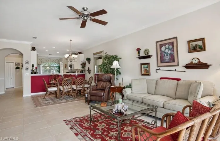 Living room featuring light tile patterned flooring, ornamental molding, and ceiling fan with notable chandelier