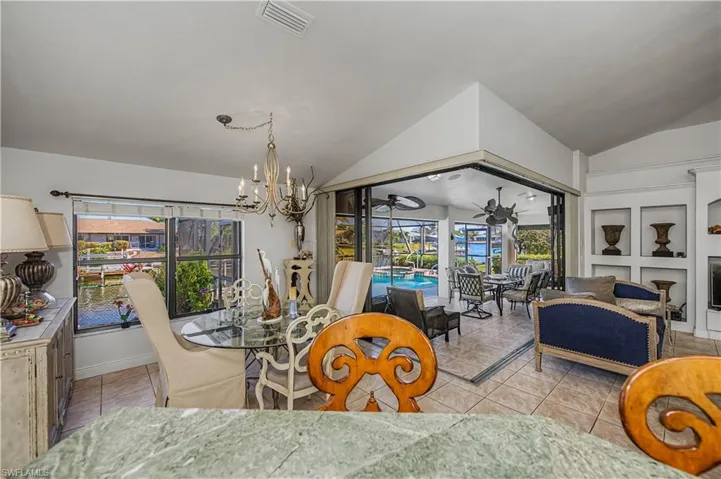 Tiled dining room with a chandelier, a sunroom, vaulted ceiling, a fireplace, and a ceiling fan
