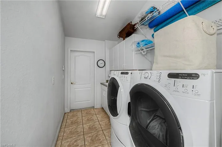 Laundry area with washing machine and clothes dryer, cabinet space, light tile patterned flooring, and a textured wall