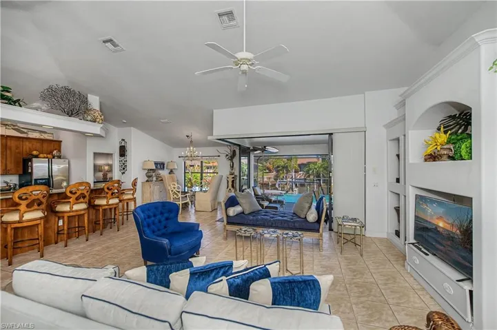 Living area with a ceiling fan, hanging lights, vaulted ceiling, built in shelves, and light tile patterned floors
