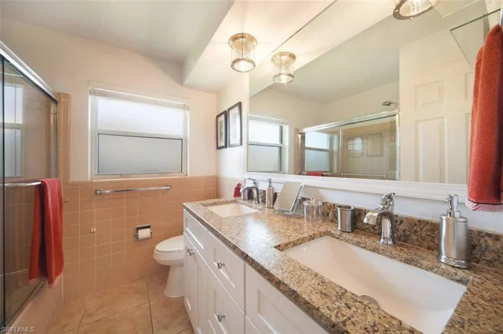 Full bathroom with double vanity, light tile patterned floors, tile walls, a wainscoted wall, and enclosed tub / shower combo