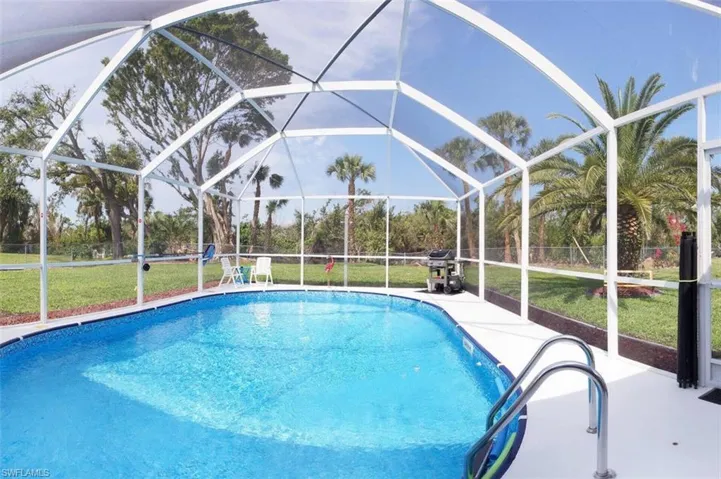 Outdoor pool with a lawn, glass enclosure, a sunroom, and a patio