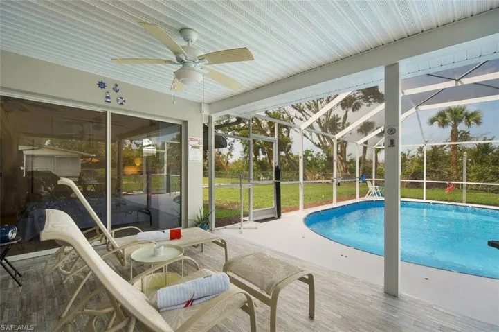 Outdoor pool with glass enclosure, a patio, a sunroom, a ceiling fan, and a lawn