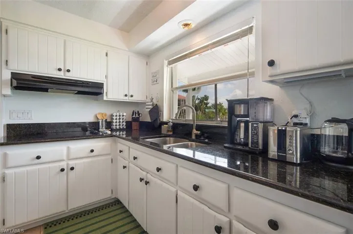 Kitchen with white cabinetry, under cabinet range hood, and dark stone countertops
