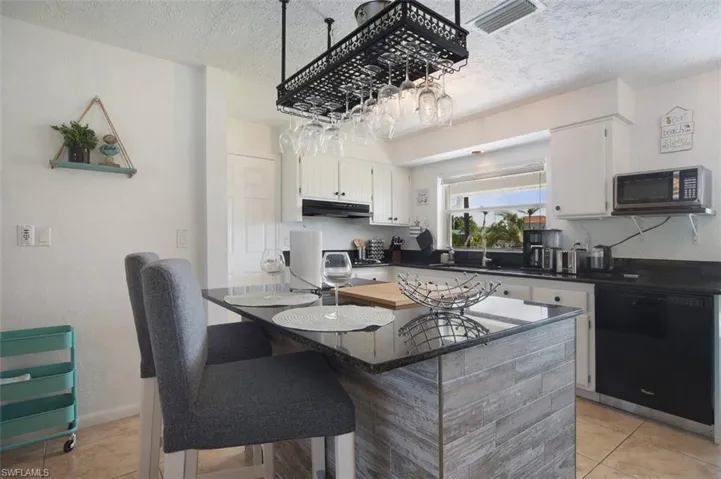 Kitchen with light tile patterned floors, a textured ceiling, dishwasher, stainless steel microwave, and a kitchen bar