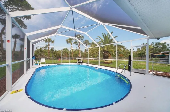 Outdoor pool featuring glass enclosure, a sunroom, a lawn, and a patio