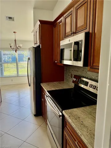 Kitchen featuring wood cabinetry, stainless steel appliances, speckled countertops, and a tiled backsplash