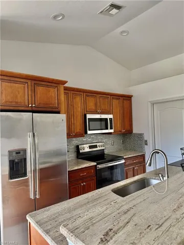 Kitchen featuring wood cabinetry, stainless steel appliances, a tile backsplash, and light-toned countertops