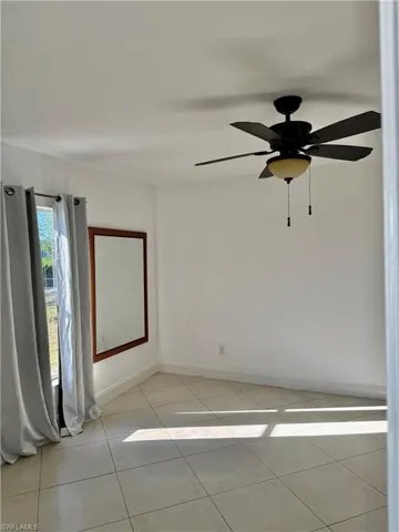 Bright room featuring large format tile flooring, white walls, a window with light gray drapes, and a ceiling fan with integrated lighting